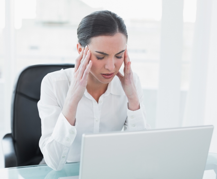 Femme assise à son bureau qui a tient la tête et qui semble être perturbée.