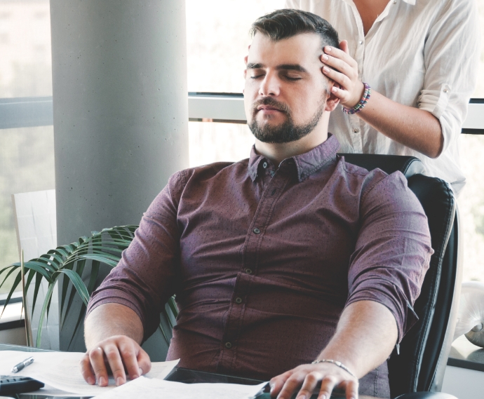 Homme assis à son bureau profitant d'une séance de réflexologie en entreprise, par la réflexologue Valérie Esquivias.